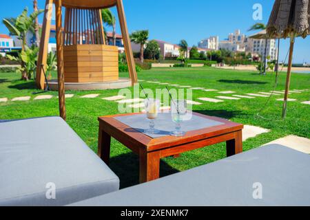 Erfrischende Getränke auf einem Resorttisch. Die Getränke sind in Gläsern und es sind Strohhalme drin. Der Tisch ist von Gras umgeben und in der Nähe befinden sich Stühle. S Stockfoto