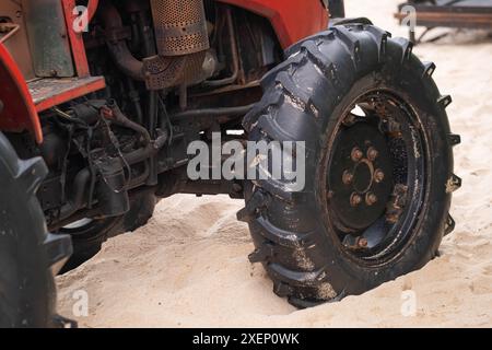 Nahaufnahme eines Traktorrads, das im Sand stecken bleibt und das Reifenprofil und den Teil des Fahrzeugs zeigt. Stockfoto