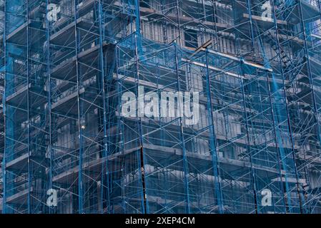 Im Bau befindliches Gebäude mit Schutzfolie aus blauem Mesh (Sicherheitsnetz bei Abbrucharbeiten), Gerüstbau in Hochhäusern, Gewerbeobjekte Stockfoto