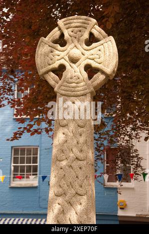 Celtic Cross, St Fimbarrus Church, Fowey, Cornwall, Großbritannien - farbige Häuser im Hintergrund und rote Blätter vom Baum. Stockfoto