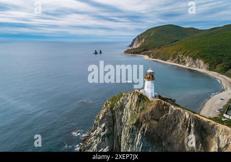 Ein Panoramablick aus der Luft zeigt den Leuchtturm von Rudnaya Pristan, der hoch auf einer zerklüfteten Klippe mit Blick auf eine malerische Bucht steht. Stockfoto