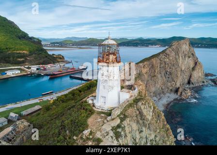 Ein Panoramablick aus der Luft zeigt den Leuchtturm von Rudnaya Pristan, der hoch auf einer zerklüfteten Klippe mit Blick auf eine malerische Bucht steht. Stockfoto