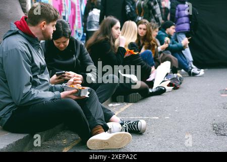 Die Schüler sitzen am Straßenrand, um ein Essen zum Mitnehmen zu genießen Stockfoto