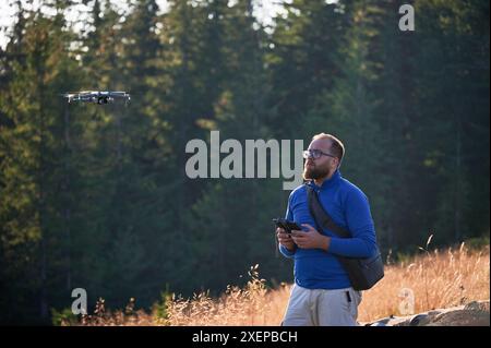 Professioneller Fotograf, der Fotos von der Drohne macht. Junger Mann, der Luftaufnahmen in den Bergen macht. Mann, der seine Drohne auf dem Hintergrund des Bergwaldes kontrolliert. Stockfoto