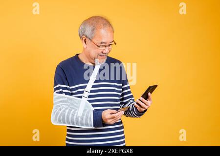 Porträt asiatischer alter Mann warf seinen Arm und hielt das Handy-Studio isoliert gelben Hintergrund Stockfoto