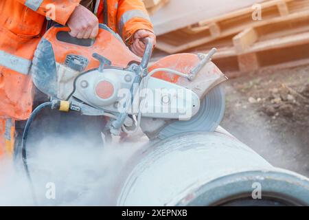 Bauarbeiter schneidet Betonrohre zur Entwässerung mit einer Trennsäge. Beim Schneiden von Beton mit einer Diamantklinge entsteht eine Wolke von Kieselsäure-Staub Stockfoto