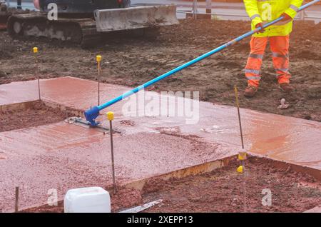 Bauunternehmen, die beim Bau von neuen Fußwegen nassen Transportbeton in Schalungen eingießen und ausebnen Stockfoto