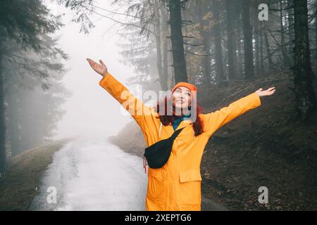 Im ruhigen Herbstwald spaziert eine einsame Frau auf einem nebelbedeckten Pfad und genießt die ruhige Schönheit der Natur während ihres Outdoor-Abenteuers. Stockfoto