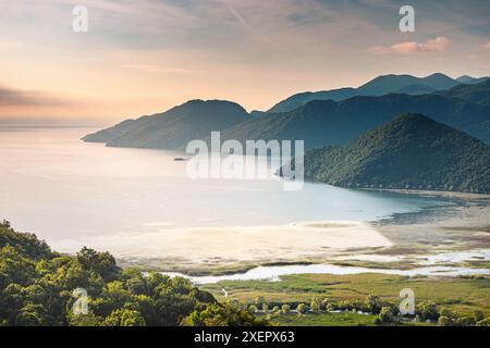 Ein wunderschöner Blick auf einen See mit Bergen im Hintergrund. Der Himmel ist eine Mischung aus Orange- und Blautönen, die eine ruhige und friedliche Atmosphäre schafft Stockfoto