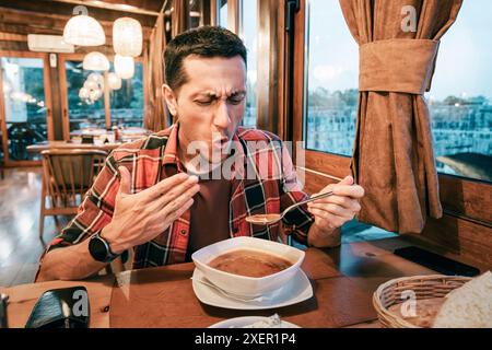 Ein Mann, der eine Schüssel mit leckerer und scharfer Suppe hält und ein befriedigendes Mittagessen genießt. Stockfoto