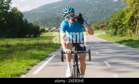 Männlicher Radfahrer, der Wasser aus der Flasche während des hochintensiven Pedalierens trinkt, Schuss verfolgt. Stockfoto