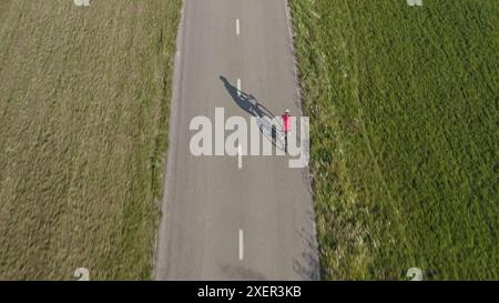 Rückansicht einer Rennradfahrerin, die auf einer leeren Asphaltstraße mit einem großen Schatten von Körper und Fahrrad fährt, Luftaufnahme einer Drohne. Stockfoto