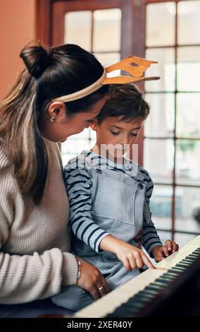 Mama, Junge und Klavier zu Weihnachten zu Hause für weihnachtslieder, Lieder oder Lernen für Musik, Aufführung oder Notizen. Mutter, Kind oder Sohn mit Tastatur zum Unterrichten Stockfoto