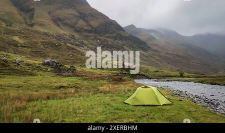 Green Zelt Wildcamping neben dem Fluss im Glen Lichd Valley, Highlands von Schottland, mit Bergen und Body im Hintergrund und stimmungsvollen niedrigen Hängen Stockfoto