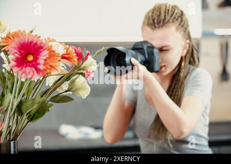 Die junge Fotografin mit geflochtenen Haaren fokussiert ihre Kamera auf einen leuchtenden Blumenstrauß. Die Blüten sind scharf im Fokus und heben ihr c hervor Stockfoto