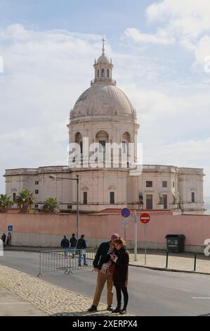Paare, die auf Telefone im Vordergrund schauen, die Panteão Nacional (Igreja de Santa Engrácia) mit ihrer beeindruckenden Kuppel im Hintergrund Stockfoto