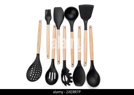 Eine Reihe von Küchenutensilien aus Holz, einschließlich Spachtel, Kelle und Schneebesen. Die Utensilien sind schwarz und hölzerne, und sie sind hintereinander angeordnet Stockfoto