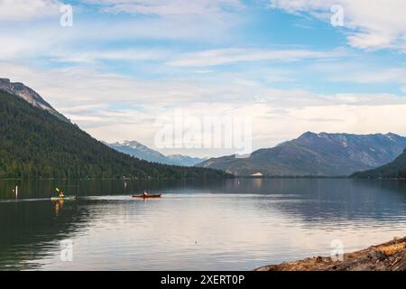 Horizontales Foto von zwei Kajakfahrern, die über das ruhige Wasser des Lake Wenatchee im Bundesstaat Washington gleiten, mit den Kaskadengebirgen im Hintergrund. Stockfoto