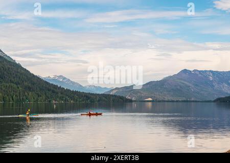 Horizontales Foto von zwei Kajakfahrern, die über das ruhige Wasser des Lake Wenatchee im Bundesstaat Washington gleiten, mit den Kaskadengebirgen im Hintergrund. Stockfoto