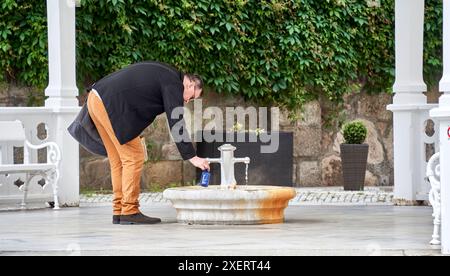 Karlsbad, Tschechien, 10. Juni 2024: Ein Mann füllt an einer öffentlichen Quelle in Karlsbad Heilwasser in eine blaue Flasche Stockfoto