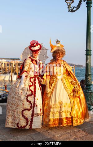 Zwei Damen in historischen Kostümen bei Sonnenuntergang, Karneval von Venedig, Venedig, Veneto, Italien posieren vor der Lagune und den Gondeln Stockfoto