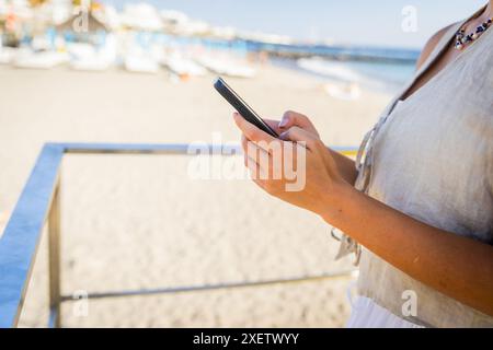 Nahaufnahme der Hände einer Frau, die ihr Smartphone am Strand benutzt. Stockfoto