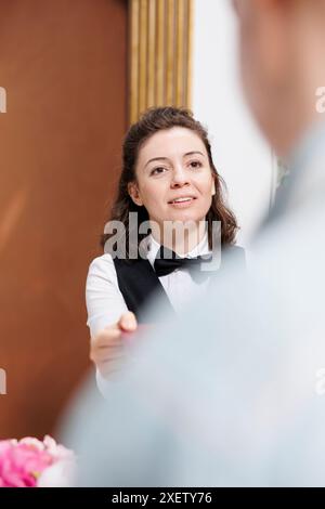 Fotofokus auf weibliche Rezeptionistin, die älteren Männern an der Rezeption beim Check-in hilft und Buchungen bestätigt. Nahaufnahme des Concierge, der den Reisepass nach der Überprüfung an den Seniorenreisenden zurückgibt. Stockfoto