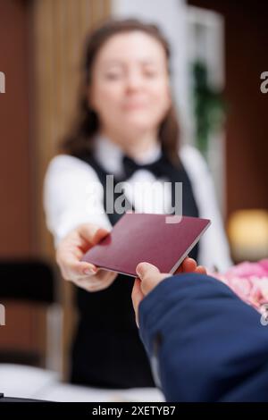 Nahaufnahme einer Concierge-Frau, die nach dem Check-in an der Rezeption einen Personalausweis an Reisende mit Winterjacke zurückgibt. Detaillierte Ansicht des Passes, den der Rezeptionist und der Tourist ergreift. Stockfoto