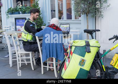 Radfahrer behandelt eine Dame am Tisch vor einem Café in der Nähe von London West End während einer Mini-Hitzewelle im Sommer England UK Stockfoto