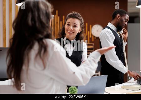 Die ältere Dame, die Touristen, meldet sich an der Rezeption der Hotellobby an, ist bestrebt, einen schönen Urlaub zu beginnen. Lächelnder junger Concierge, der Seniorinnen im Ruhestand Tipps für die besten Urlaubsaktivitäten gibt. Stockfoto
