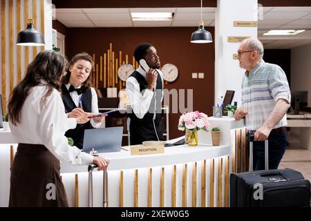 Hotelrezeptionisten helfen älteren Reisenden beim Check-in an der Rezeption. Dankbare Seniorin unterschreibt Dokumente mit Lächeln, während das Personal für einen reibungslosen Ablauf sorgt. Außergewöhnlicher Kundenservice. Stockfoto