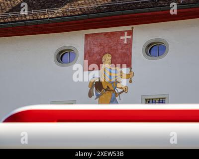 Schwyz, Schweiz - 18. Juni 2024: Mittelalterliche Figur mit roter Flagge des schweizer Kantons Schwyz, Fassade des Schweizerischen Nationalmuseums. Stockfoto