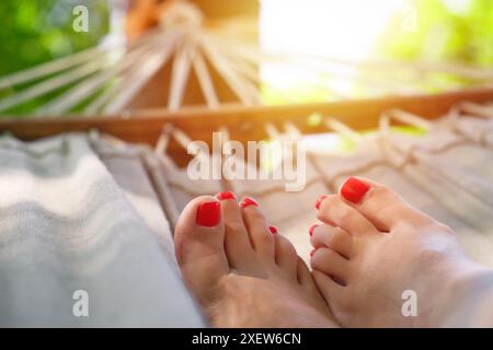 Nahaufnahme von Frauenbeinen mit rotem nagellack auf Hängematte. Frau, die sich am sonnigen Sommertag auf einer Hängematte ausruht. Entspannungs- und Urlaubskonzept. Stockfoto