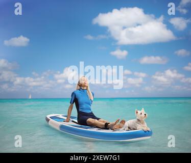 Frau mit einem Hund, der auf einem Brett im Meer sonnt Stockfoto