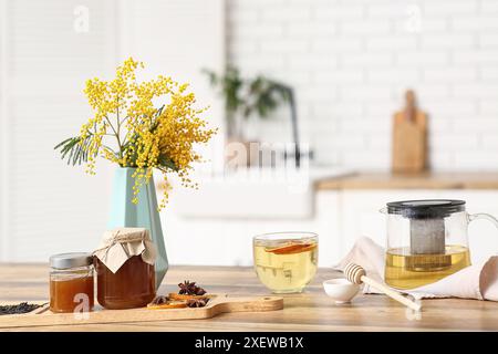 Teekanne und Tasse grünen Tee mit einem Glas Honig und Mimosa auf dem Tisch in der Küche Stockfoto