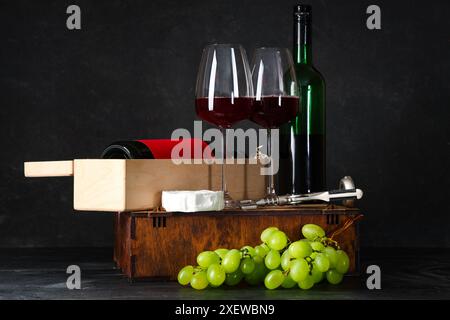 Boxen mit Flaschen Wein, Gläsern, Trauben und Camembert-Käse auf schwarzem Grunge-Hintergrund Stockfoto