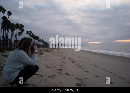 Frau fotografiert einen ruhigen Strand bei Sonnenuntergang. Stockfoto