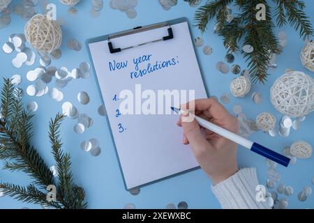 Unerkennbare Frau, die Neujahrsvorsätze auf Papier mit Weihnachtsdekor schreibt. Versprechen für das neue Jahr machen, Ziele setzen. Motivation für Vision Board schaffen Stockfoto