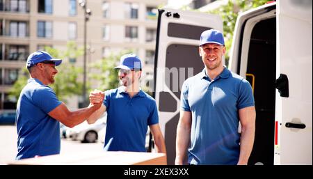 Effizienter Umzugsservice durch professionelle Umzugswagen: Mann in Uniform liefert Pakete mit einem Lächeln vor seinem Van. Stockfoto