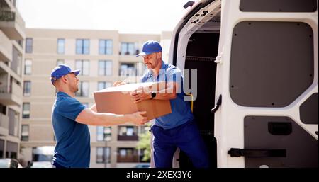 Erfahrene Umsteiger in Aktion: Erfahrene kaukasische Männer laden Kisten in den Lieferwagen, um effiziente Umzugsdienste zu gewährleisten. Teamarbeit und Professionalität Stockfoto