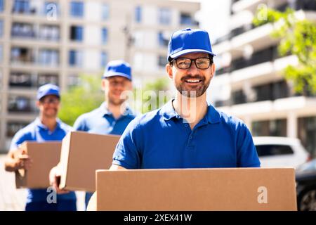Professionelle Liefermänner transportieren Pappkartons am sonnigen Tag effizient vor dem LKW des Unternehmens Stockfoto