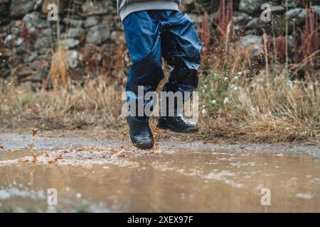 Ein Kind springt in den Regen und spritzt überall Wasser. Die Szene ist verspielt und fröhlich, während das Kind den Regen genießt und Spaß hat Stockfoto