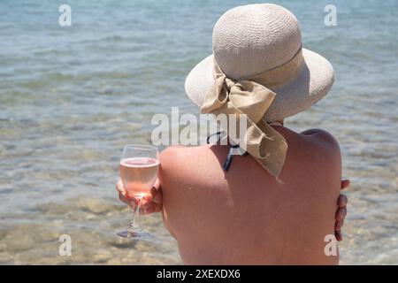 Frau mit Hut und Glas Champagner am Strand. Stockfoto