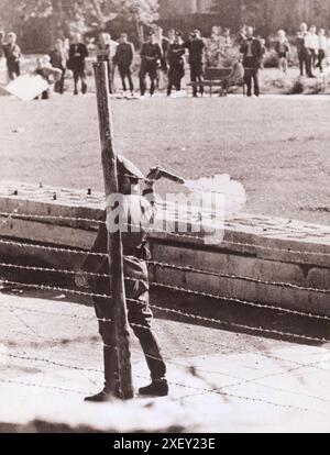 Vintage-Foto der Berliner Krise von 1961: Mauerbau. Kommunistische Volkspolizisten, die zwischen Grenzzaun und Mauer stehen, bereiten sich darauf vor, eine Tränengasgranate auf eine Gruppe von Westberlinern zu werfen, die sich auf ihrer Seite der Grenze versammelten, um die Roten Garde zu verhöhnen. West-Berlin. Oktober 1961 Stockfoto