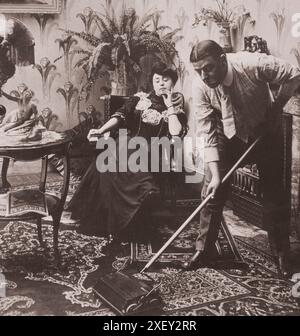 Vintage-Foto der Liebe. „Nehmen Sie sich Zeit, Herr Peck – Eile macht Verschwendung“. USA. 1907 Mann mit Teppichkehrer, als Frau sitzt und zuschaut. Stockfoto