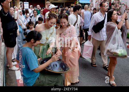 Thailändische Touristen in der Altstadt von Phuket in traditioneller thailändischer Tracht und sprechen mit einem Straßenmusiker, der eine Handpfanne spielt, einer Handtrommel aus Metall Stockfoto