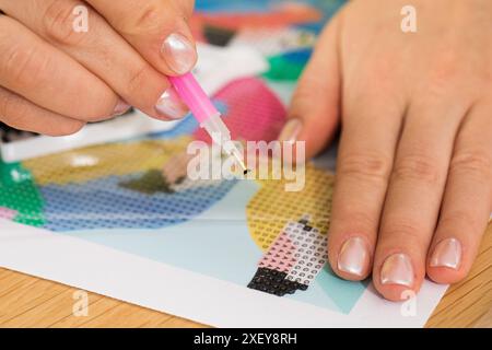 Eine Nahaufnahme einer Hand, die Kristalle auf einer Leinwand für ein Diamantmalprojekt platziert. Diamantmosaik Stockfoto