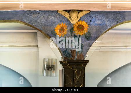 Ein geschnitzter Engelskopf mit zwei gemalten Sonnenblumen schmückt einen Pfeiler der Zion-Kirche in Worpswede, erbaut 1757 bis 1759. Die Wandgemälde an den Galeriepfeilern wurden 1900 als gemeinsame Buße von der Malerin Paula Modersohn-Becker und der Bildhauerin Clara Westhoff geschaffen, nachdem die beiden ohne Erlaubnis die Kirchenglocken geläutet und das Dorf erschreckt hatten. Der Tradition nach schnitzte Westhoff die Engelsköpfe, während Modersohn-Becker die floralen Spiegelbögen, wie die abgebildeten Sonnenblumen, malte. Worpswede, Niedersachsen, Deutschland. Stockfoto