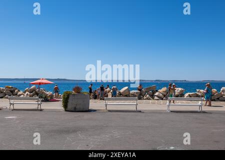 Piran, Slowenien - 20. Juli 2022: Menschen an der Strandpromenade mit Bänken in einem Kurort an der Adria an der Südwestküste Sloweniens. Stockfoto