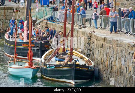 Besucher des Portsoy Boat Festival besuchen und beobachten die Boote, die im alten Hafen vor Anker liegen Stockfoto